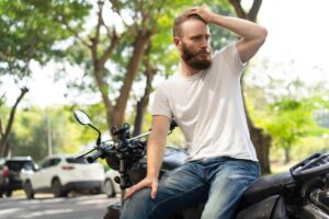 Ragazzo senza casco seduto su una moto che si tiene la mano sulla testa