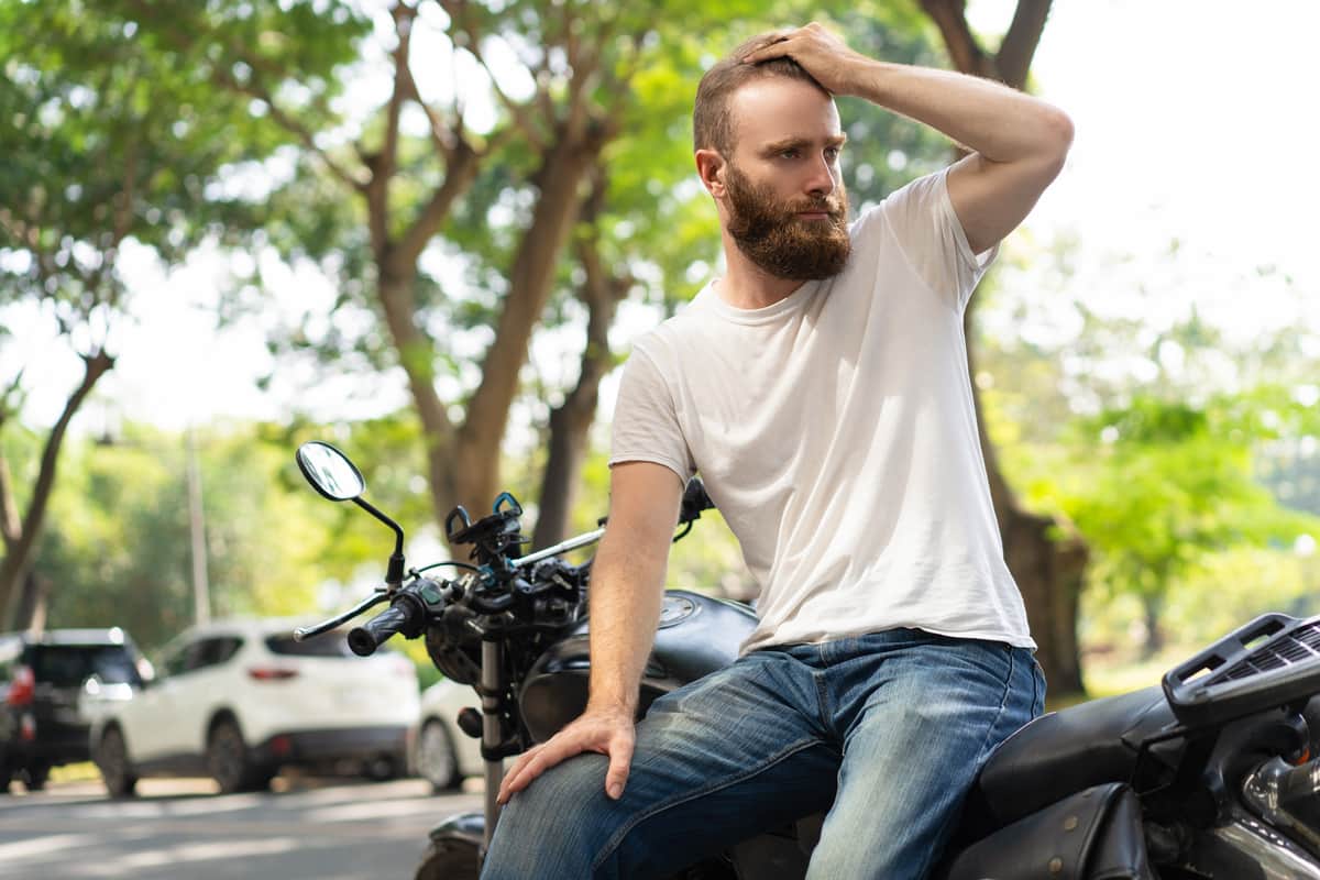 Ragazzo senza casco seduto su una moto che si tiene la mano sulla testa